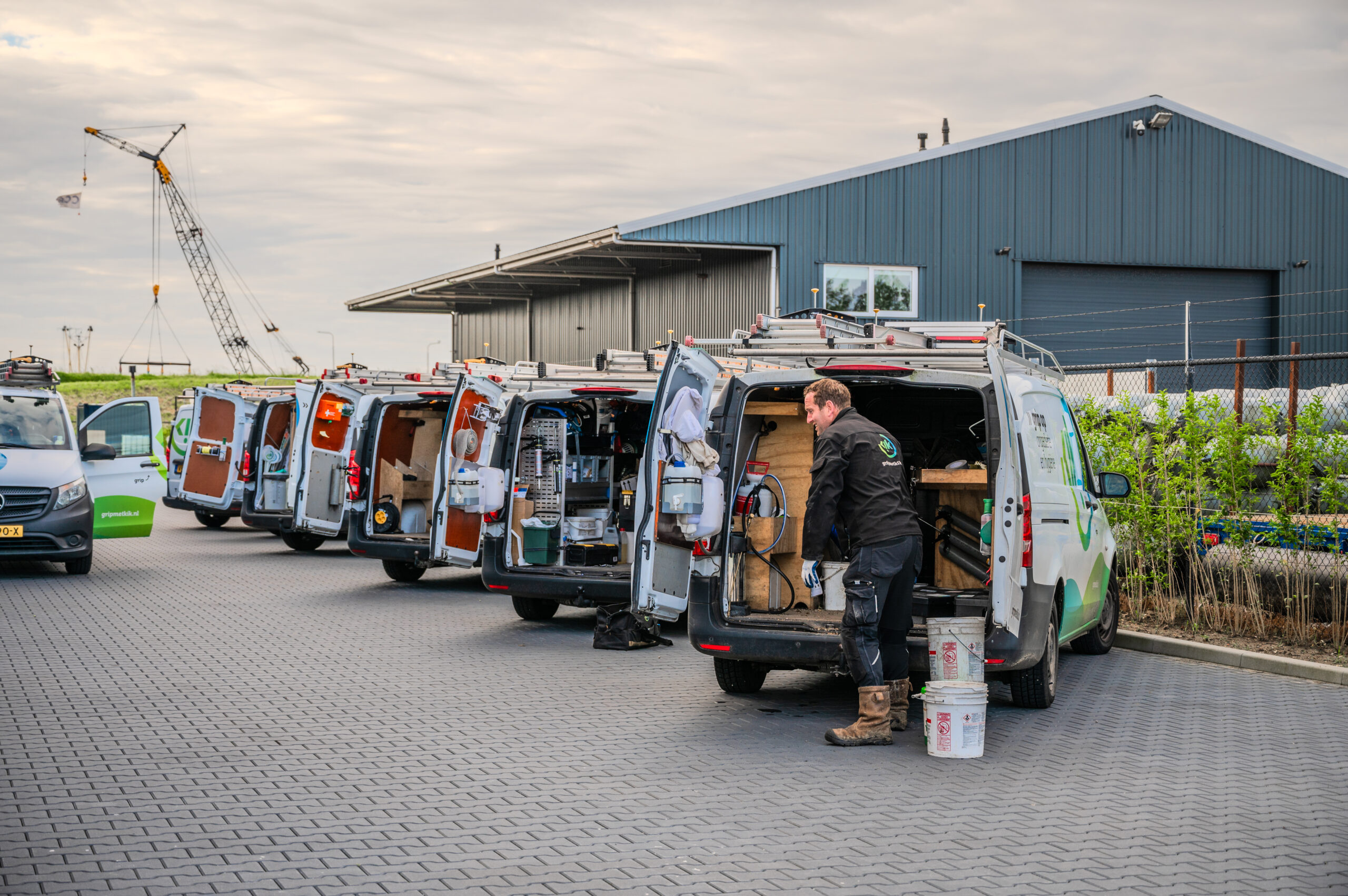 Meerdere Kik-service-busjes staan geparkeerd bij een bedrijfspand terwijl een technicus uitrusting uitlaadt voor zakelijke ongediertebestrijding.